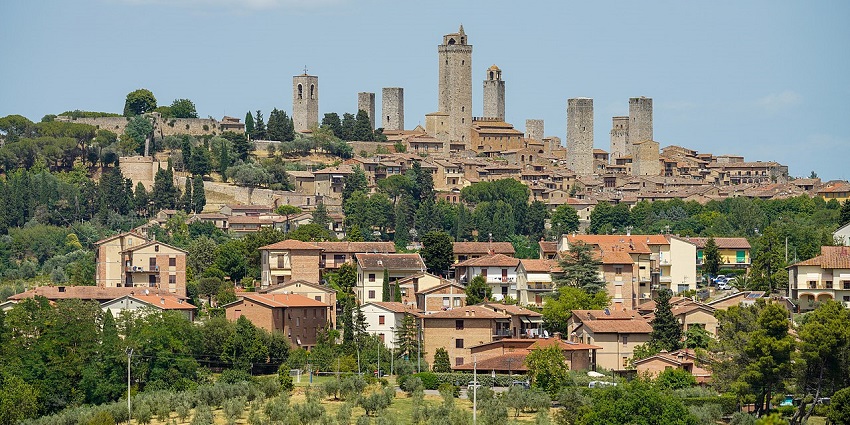 Hilltop medieval townscape with tall stone towers rising above rustic houses and trees, one of the best places to visit near Florence.
